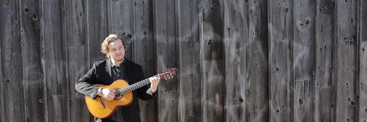 Joseph Douglass standing and holding his guitar.