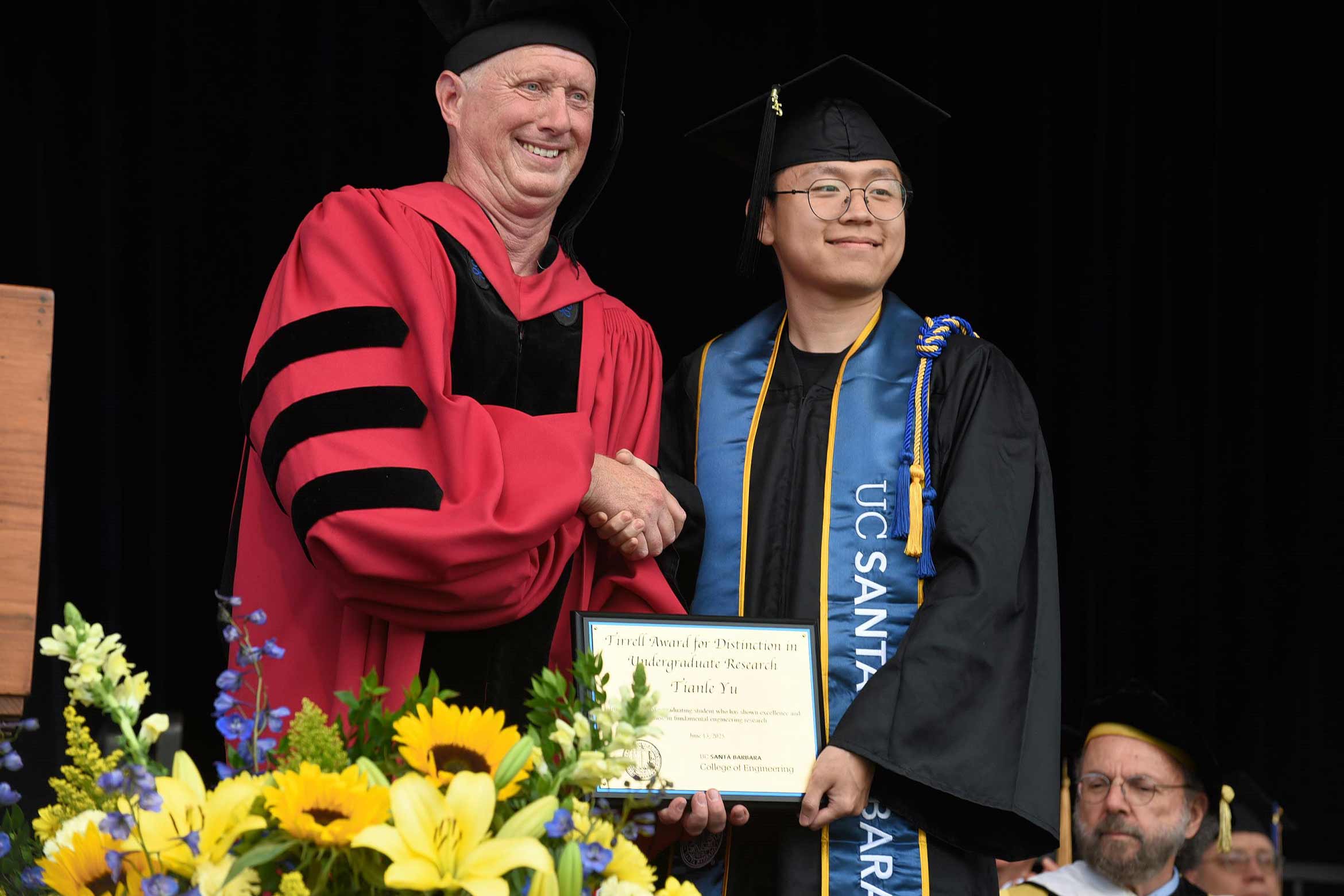 Tianle-Yu, in cap and gown, shaking hands with a faculty member while receiving a Tirrell Award